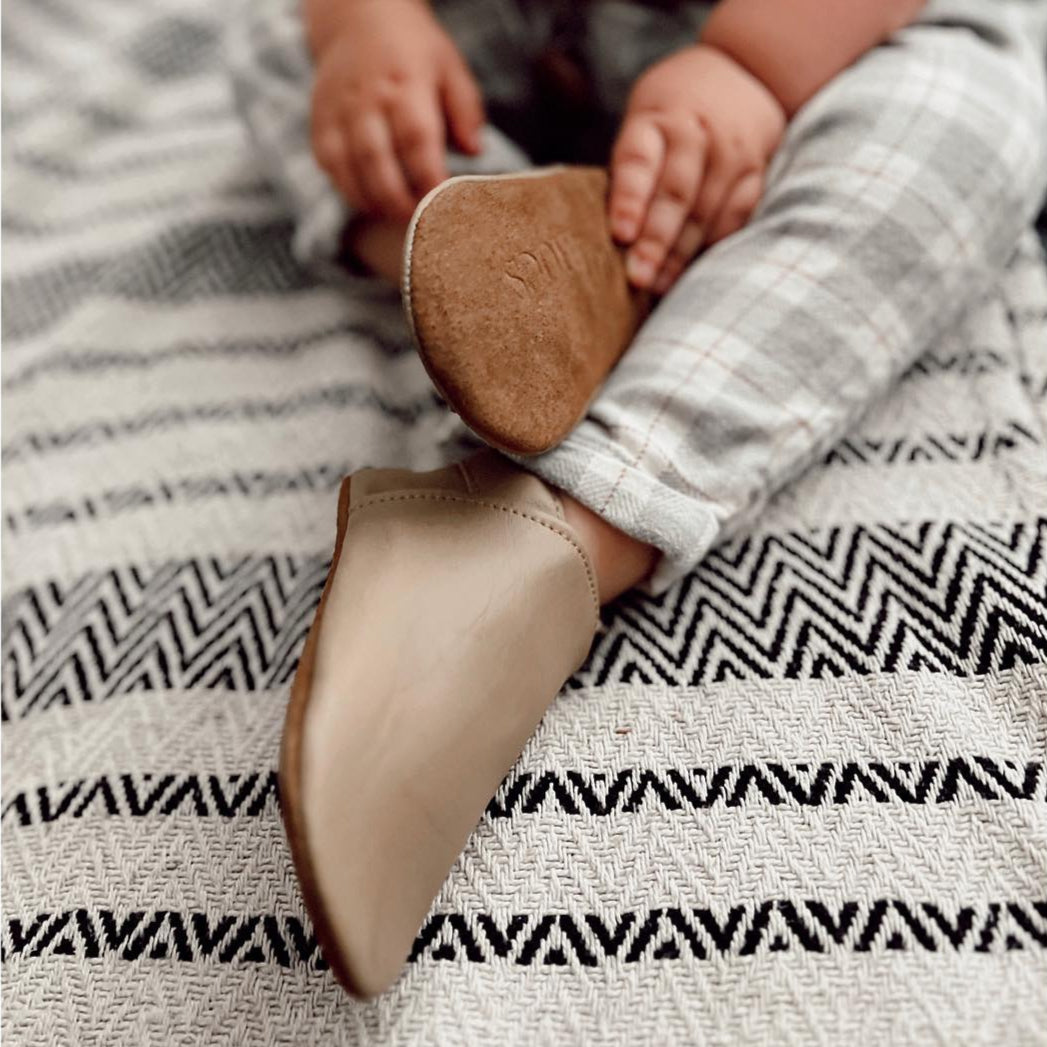 Child's feet wearing brown and beige shoes on a patterned blanket