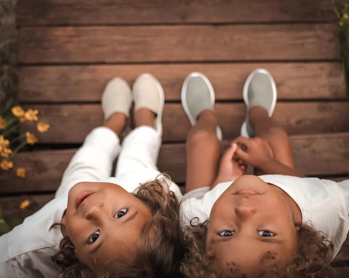 Two children standing on a wooden floor, looking directly at the camera.